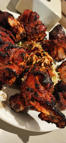 Grilled chicken pieces sizzling on a rustic wooden platter with herbs.