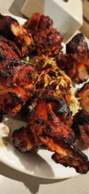 Grilled chicken pieces with a charred exterior served on a white plate, accompanied by a garnish of mixed sprouts and shredded vegetables.
