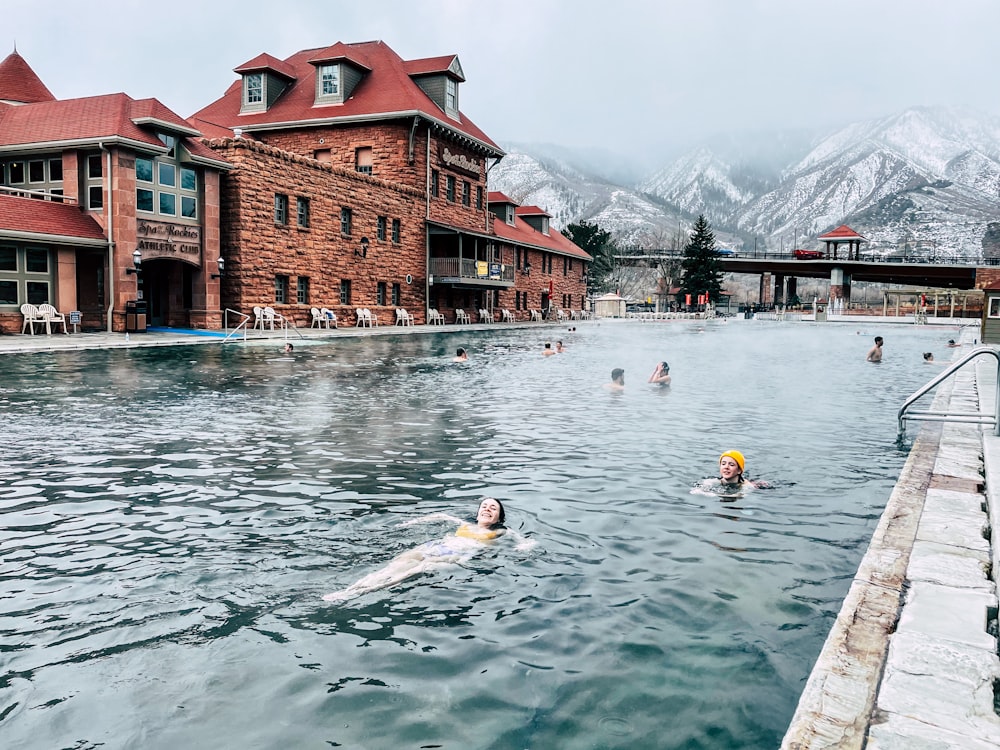 people swimming on the river near the red and brown concrete building during daytime