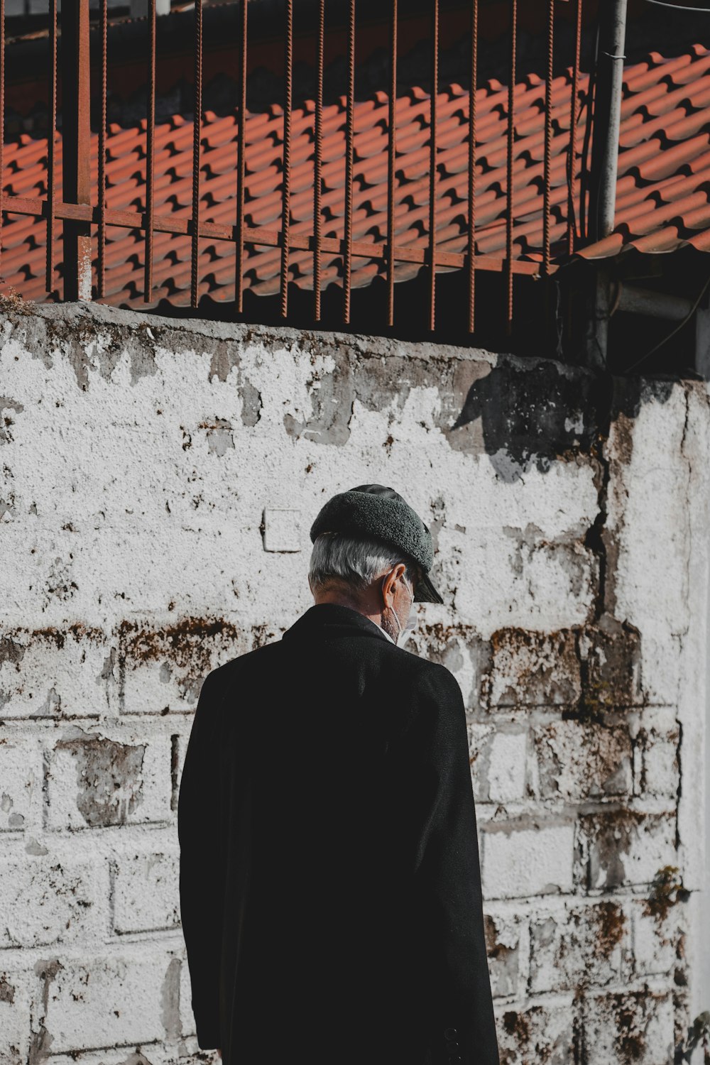 man in black suit standing beside white concrete wall during daytime