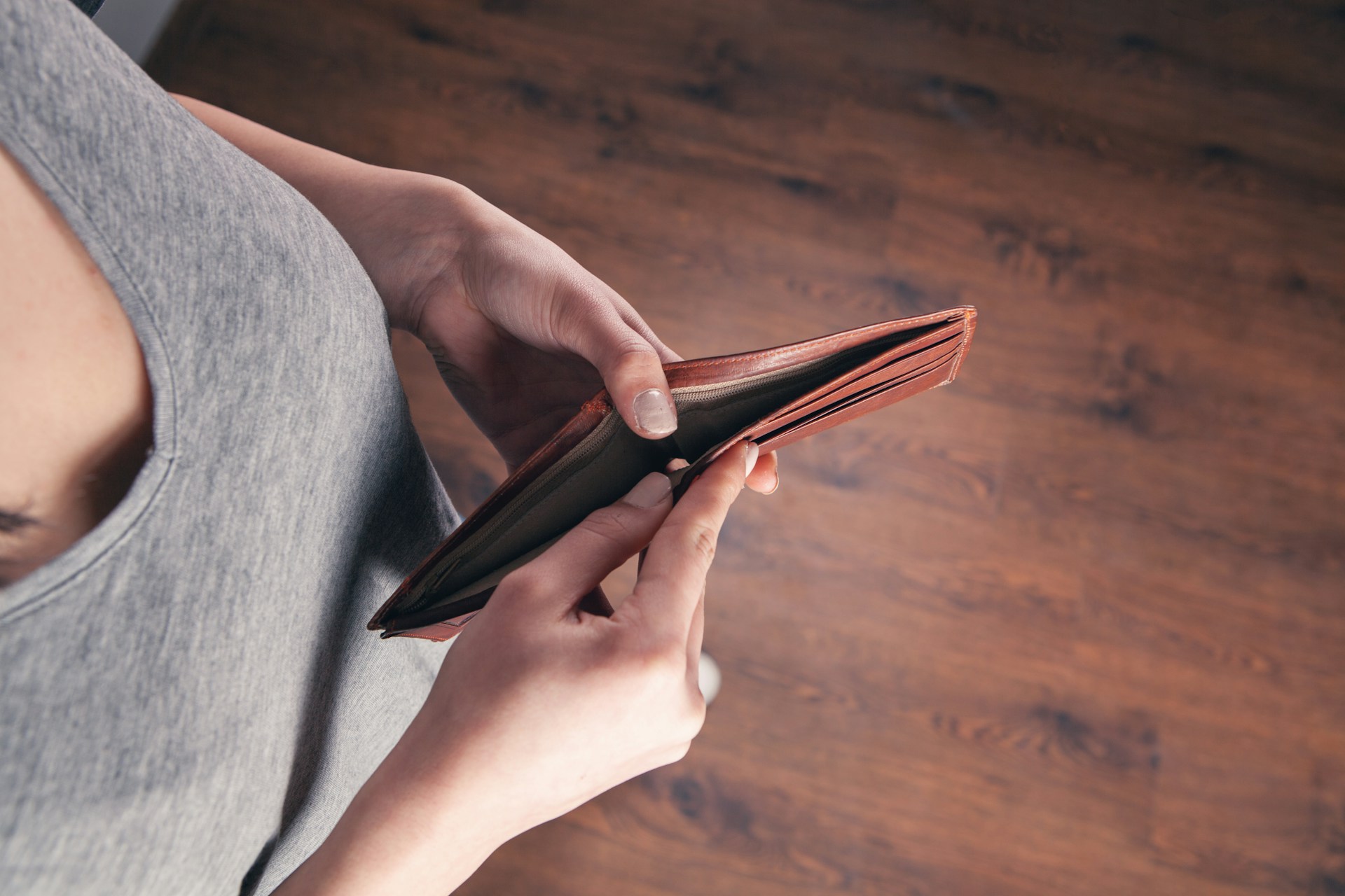 Close-up of hands holding an empty wallet with a blurred background of overdue bills and invoices.