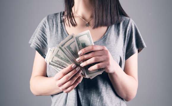 woman in gray shirt holding fan of us dollar bills