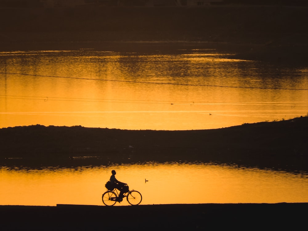 silhouette of 2 people riding bicycle on seashore during sunset