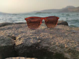 Wild sunglasses resting on a rock beside a flowing river under bright daylight.