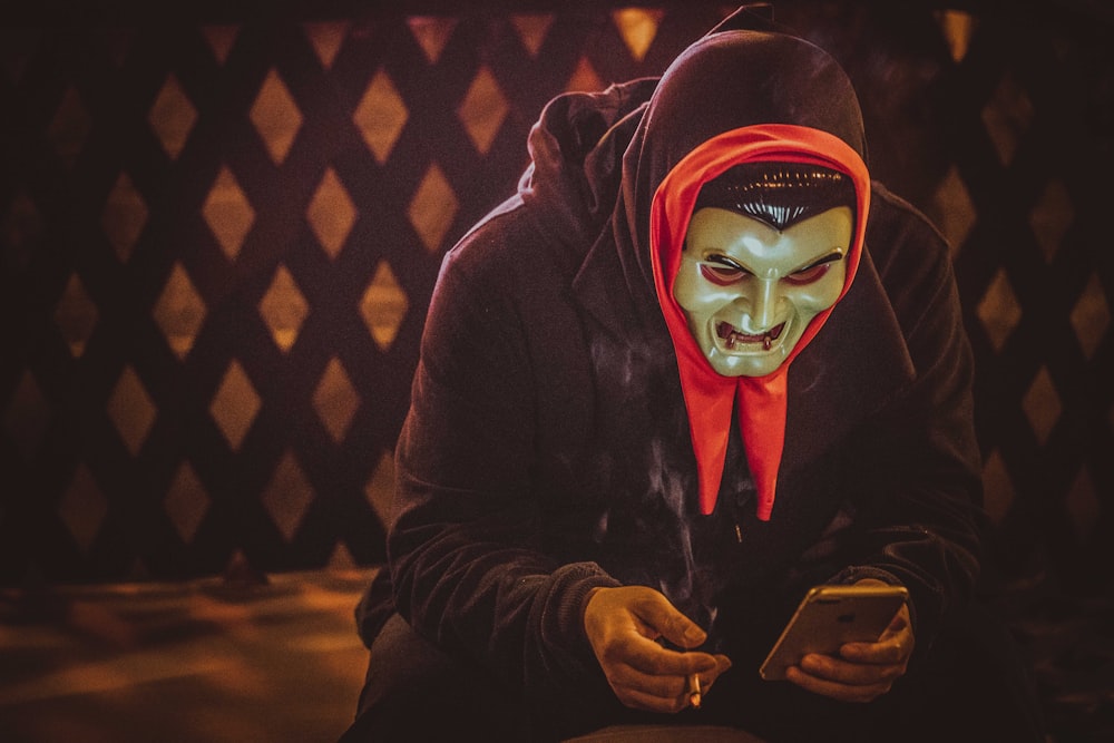 person in black and red mask holding smartphone