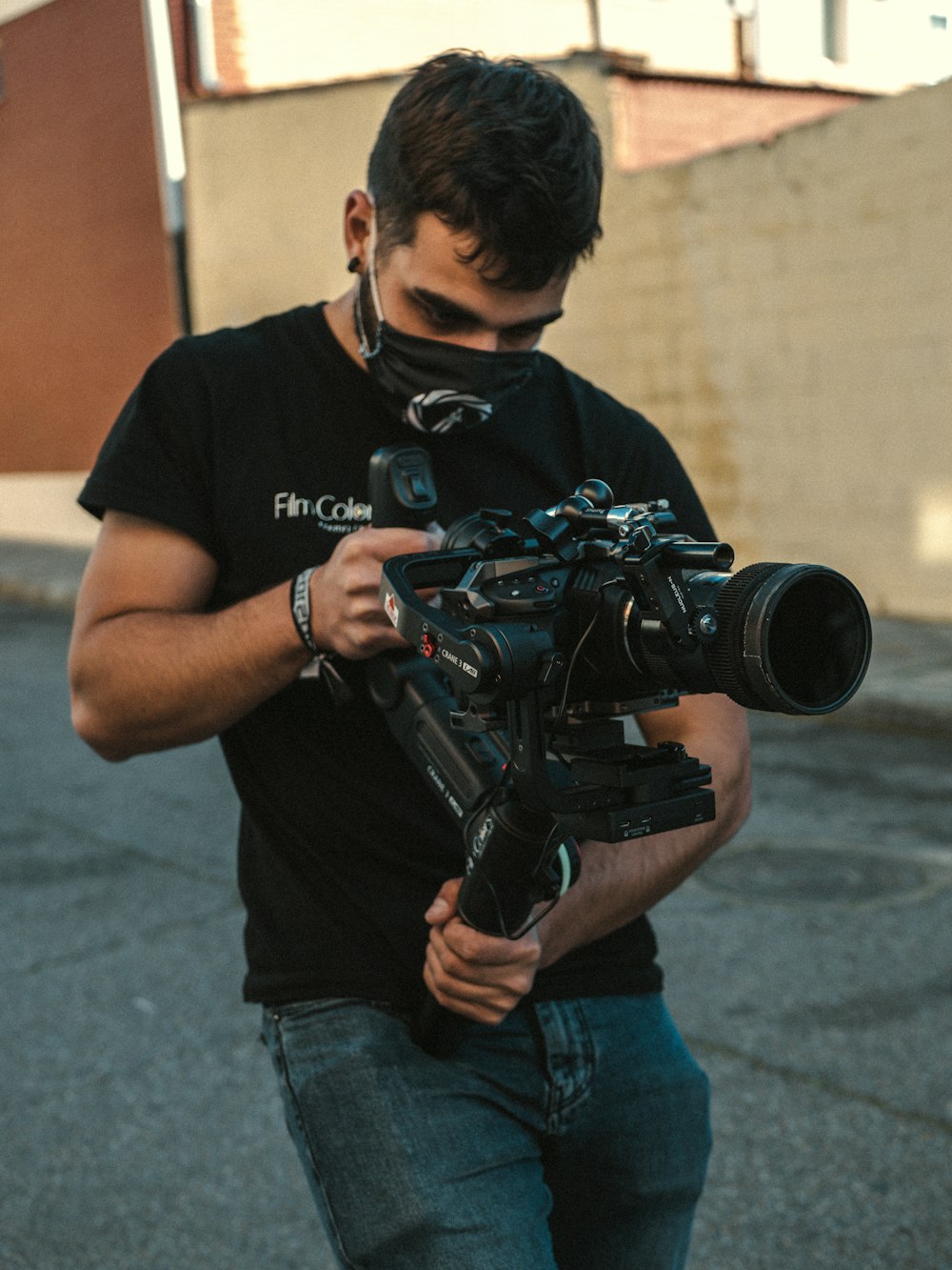 Uomo in t-shirt girocollo nera e jeans blu in denim con fotocamera DSLR nera