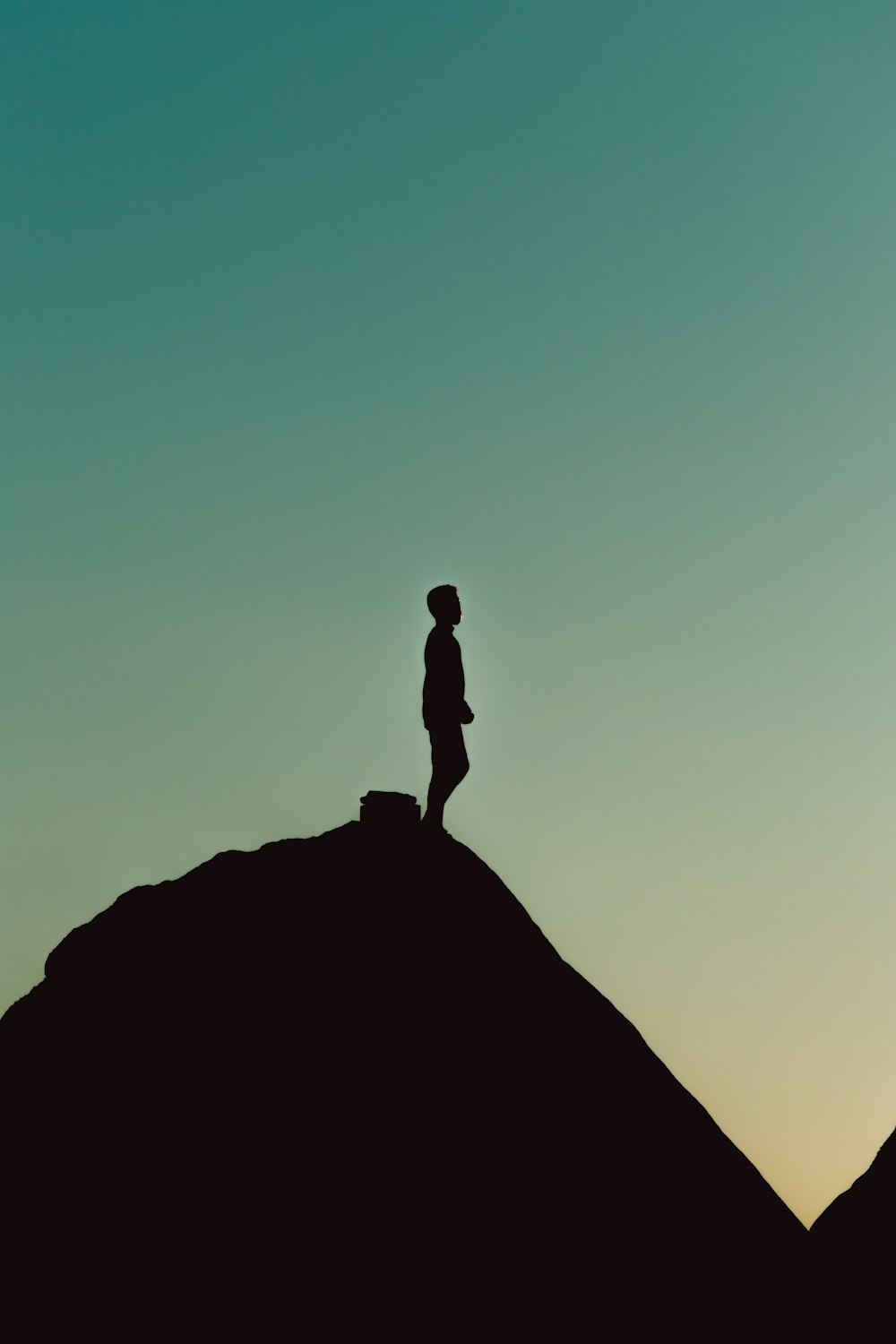 silhouette of man standing on rock formation during daytime