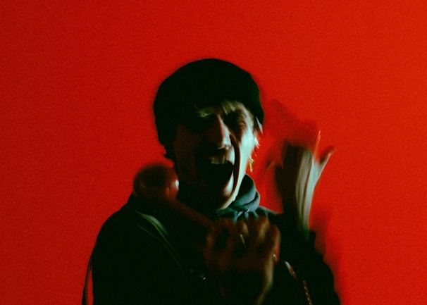 A person is holding a phone receiver against a vibrant red background, appearing animated with blurred motion.