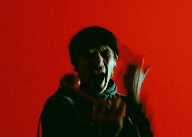 A person is holding a phone receiver against a vibrant red background, appearing animated with blurred motion.