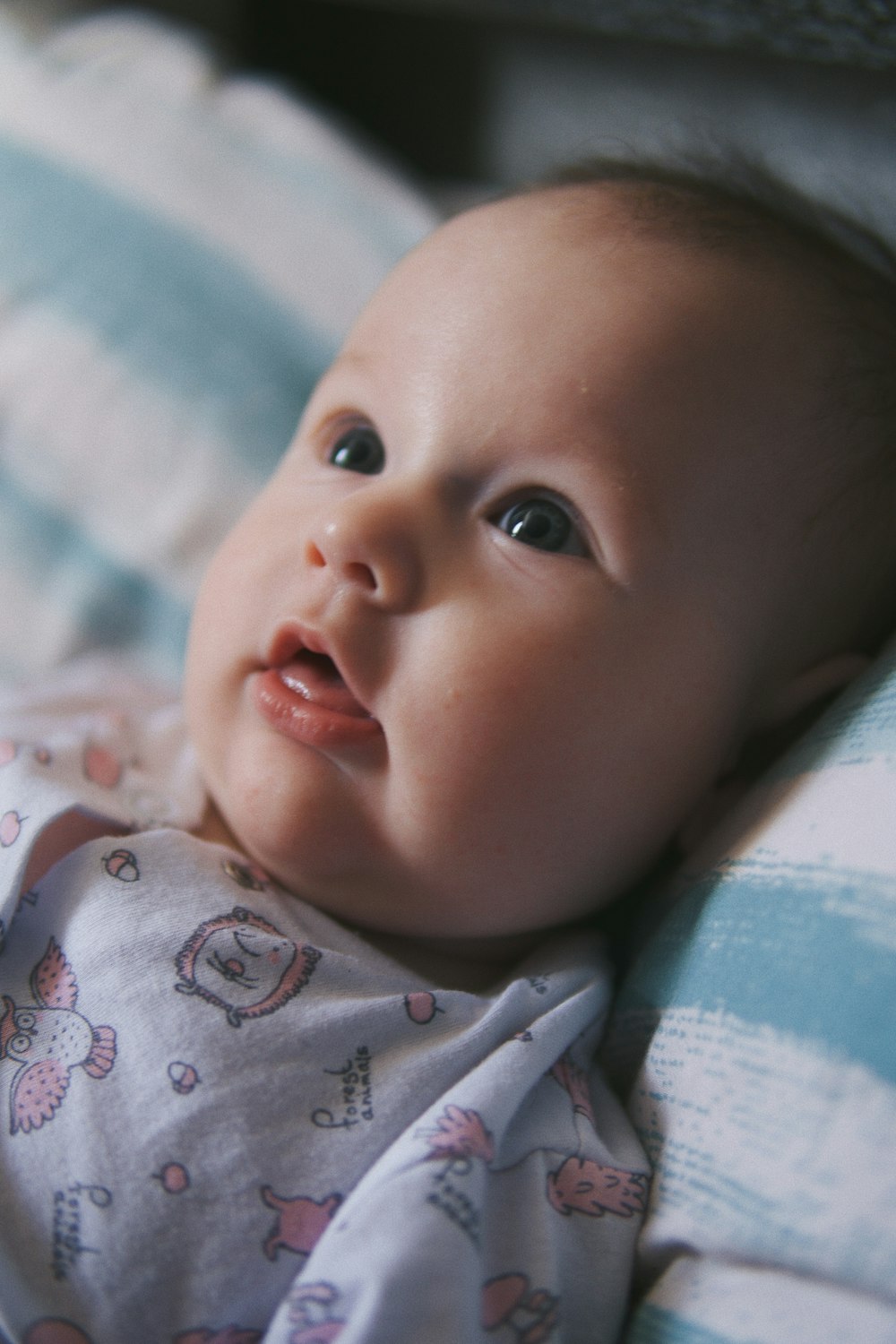 Baby in weißem und blauem Onesie liegt auf dem Bett