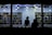 Silhouetted figures appear inside a well-lit bookstore, standing behind a counter with various books. The walls are lined with shelves filled with a diverse array of books, creating a vibrant backdrop. Ceiling lights cast a bright glow, highlighting the books and the interior.
