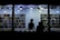 Silhouetted figures appear inside a well-lit bookstore, standing behind a counter with various books. The walls are lined with shelves filled with a diverse array of books, creating a vibrant backdrop. Ceiling lights cast a bright glow, highlighting the books and the interior.