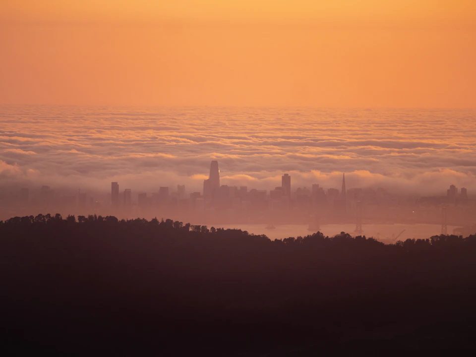 City skyline at sunset with sun setting behind horizon casting warm orange glow