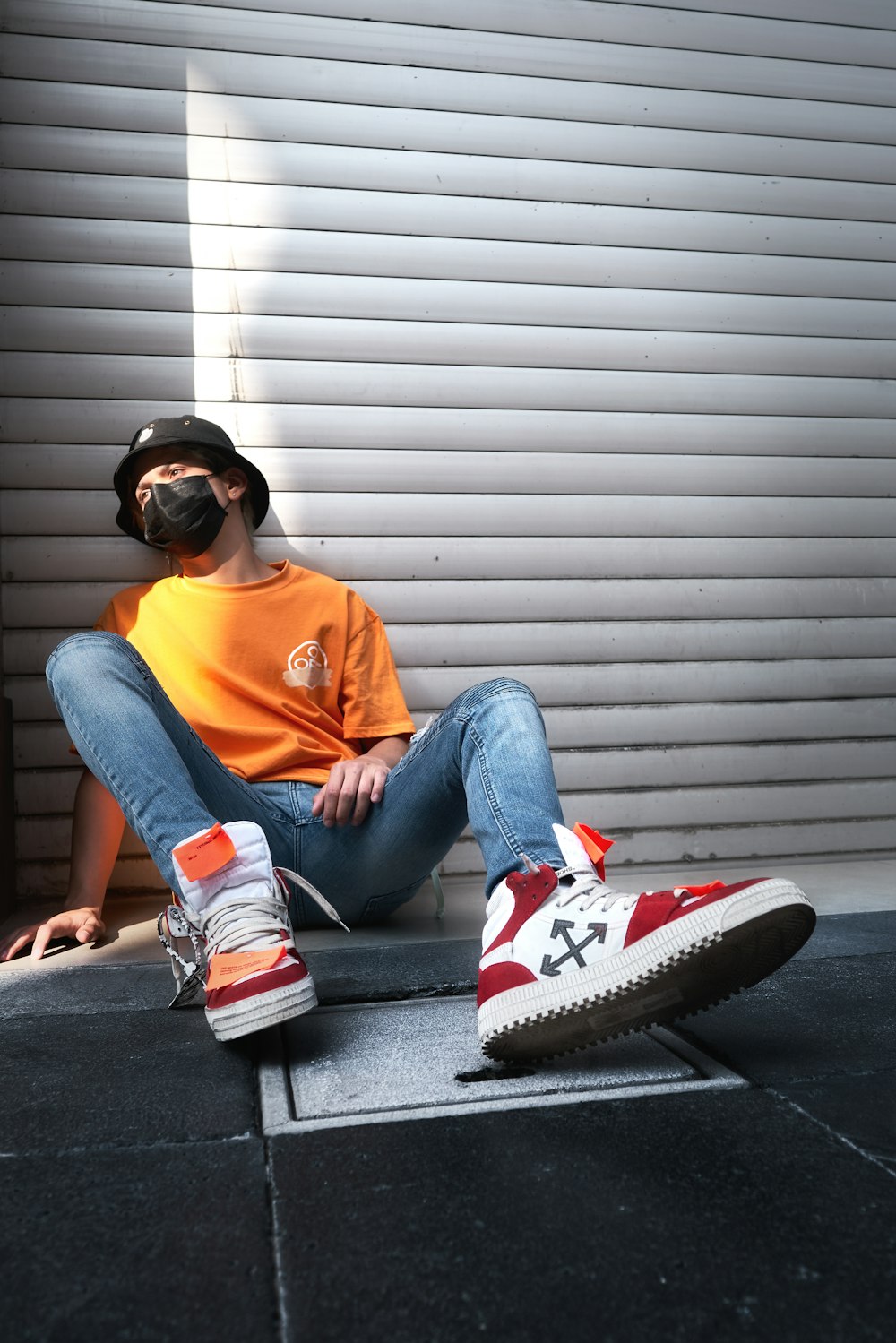 woman in orange crew neck t-shirt and blue denim jeans sitting on gray concrete stairs