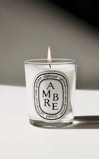 Close-up of a minimalist glass candle with a deep aubergine label softly glowing in a dark room.