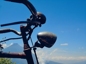 A close-up of a weathered bicycle handlebar resting against a rugged mountain backdrop at sunrise.