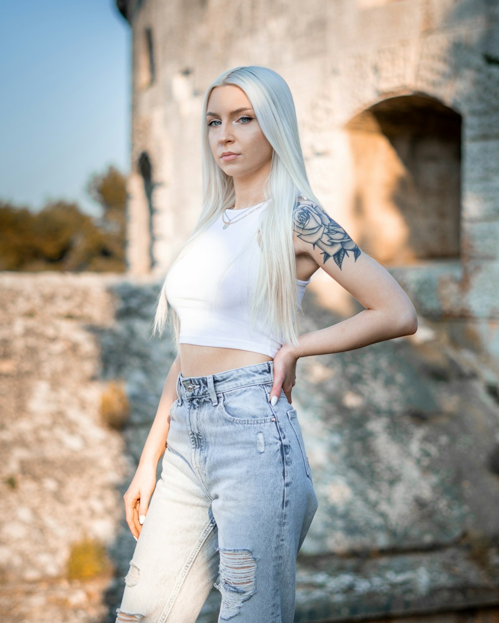 woman in white tank top and blue denim shorts standing near brown wall during daytime