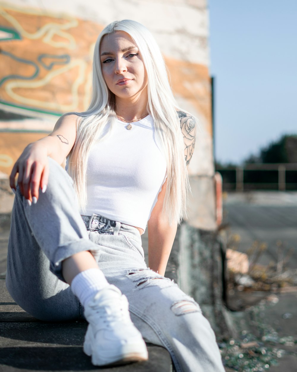 woman in white tank top and gray pants sitting on gray concrete floor during daytime