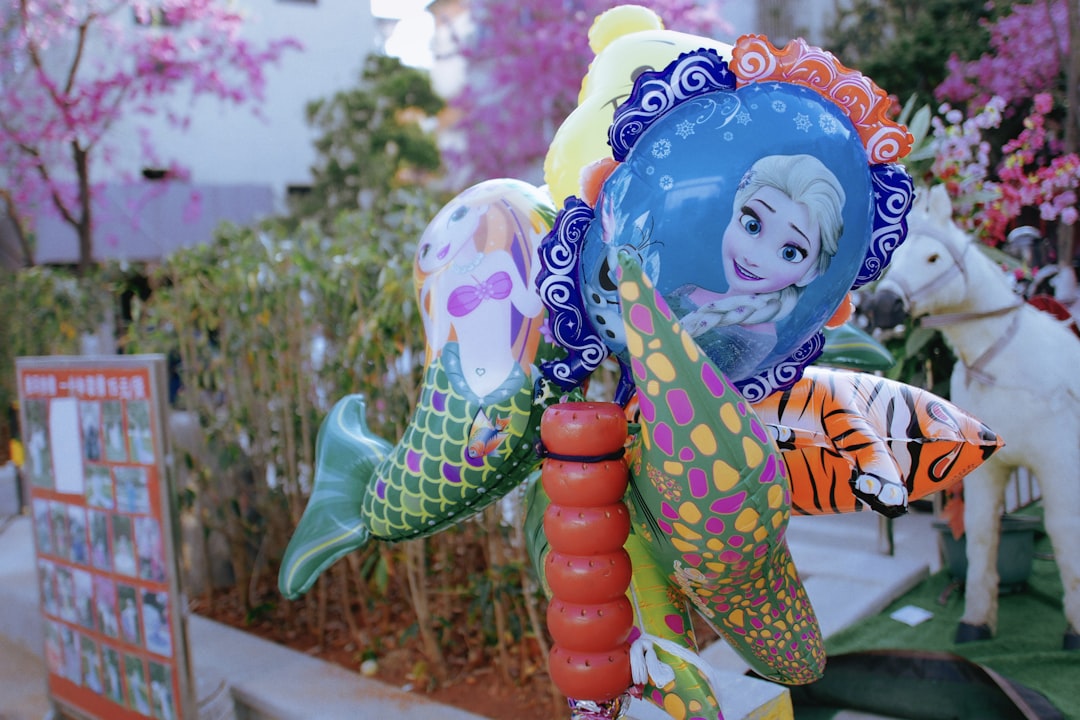 girl in blue and yellow dress holding green and pink balloons,