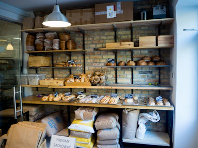 Close-up of various bags of flour stacked neatly on wooden shelves in a cozy bakery supply store.
