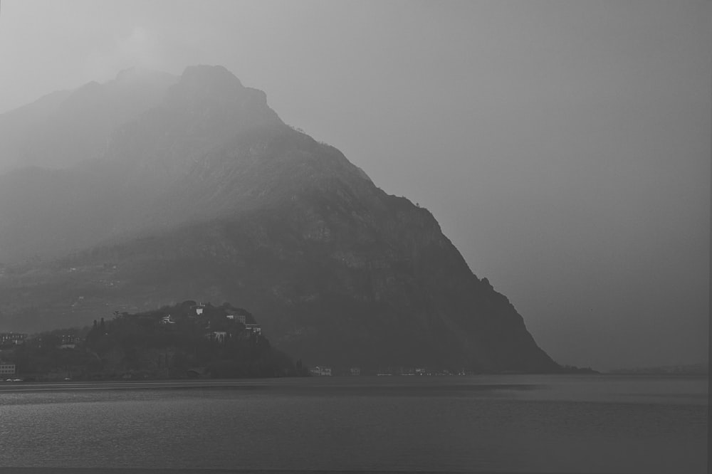 body of water near mountain during foggy weather