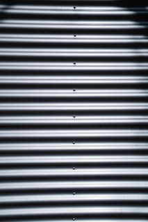 Corrugated metal sheet with horizontal ridges and bolts aligned vertically in the center.