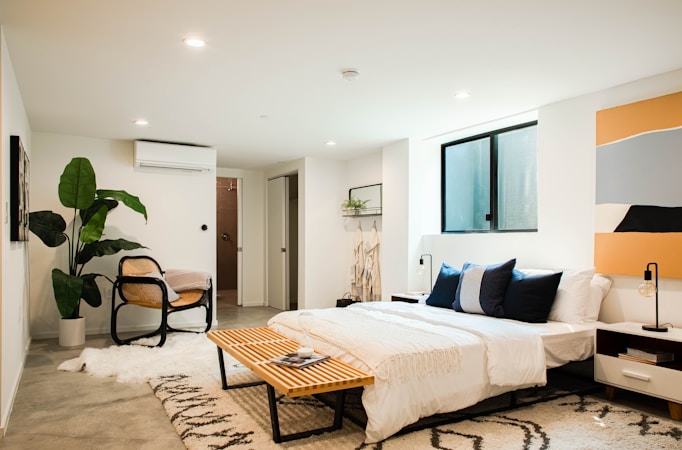 Modern bedroom featuring a large bed, wooden bench, chair, and decor; ideal for alternative student 
