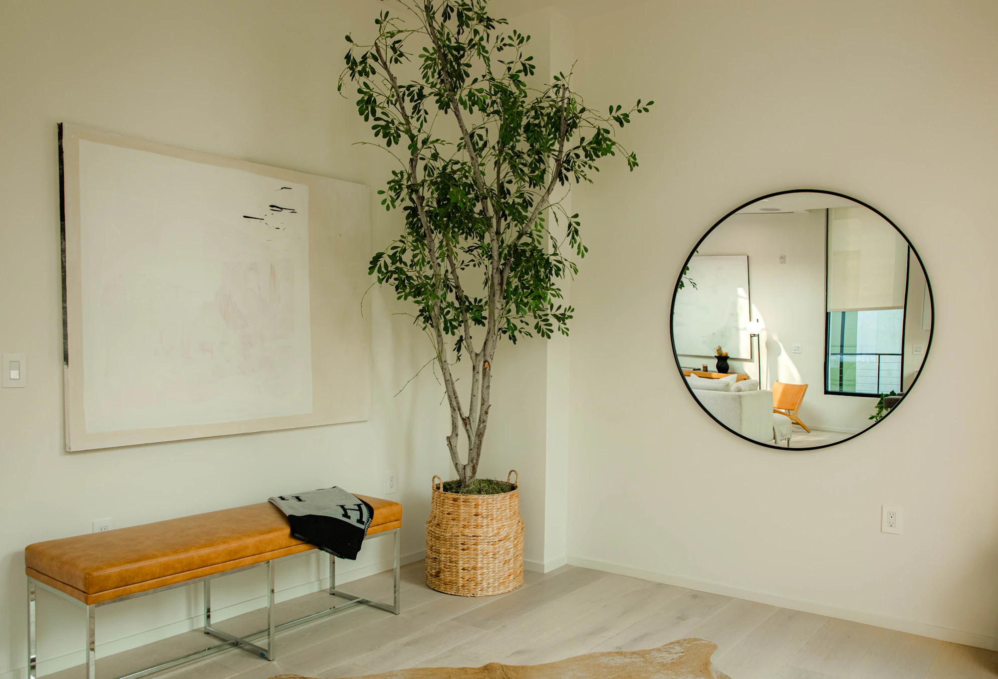 A bright, calm room with a round wall mirror, a padded bench and a potted tree (stand-in for a consultation space)