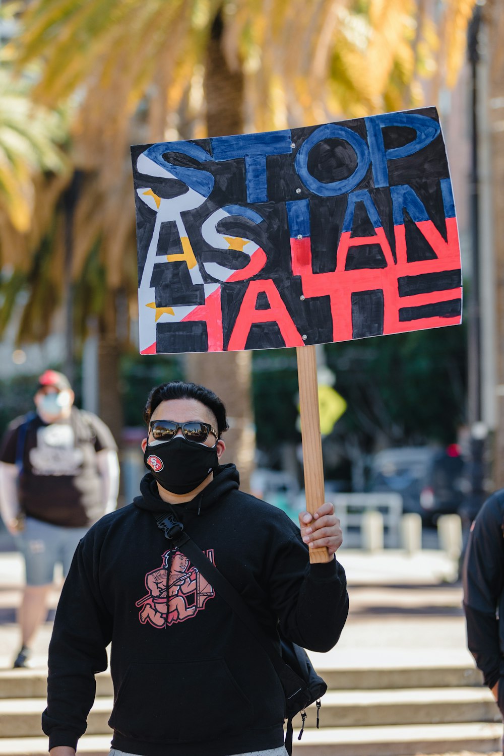 man in black hoodie holding blue and white no smoking sign