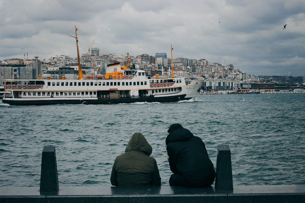 man in black hoodie sitting on the edge of the boat looking at the city during