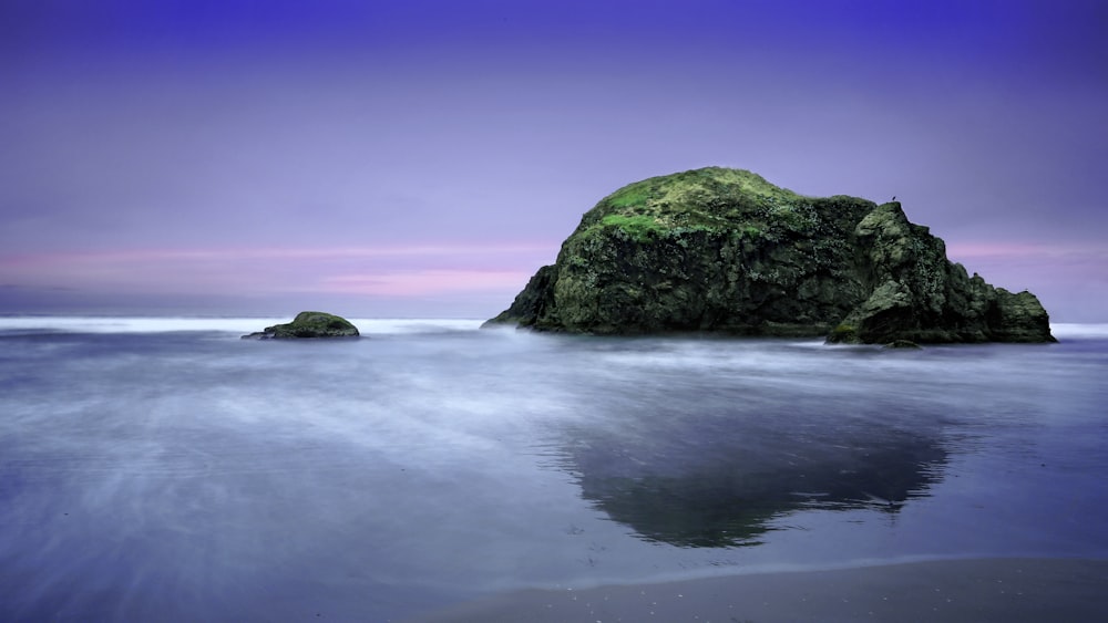 green and black rock formation on sea under blue sky during daytime