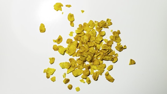 A pile of golden cornflakes scattered across a smooth white surface.