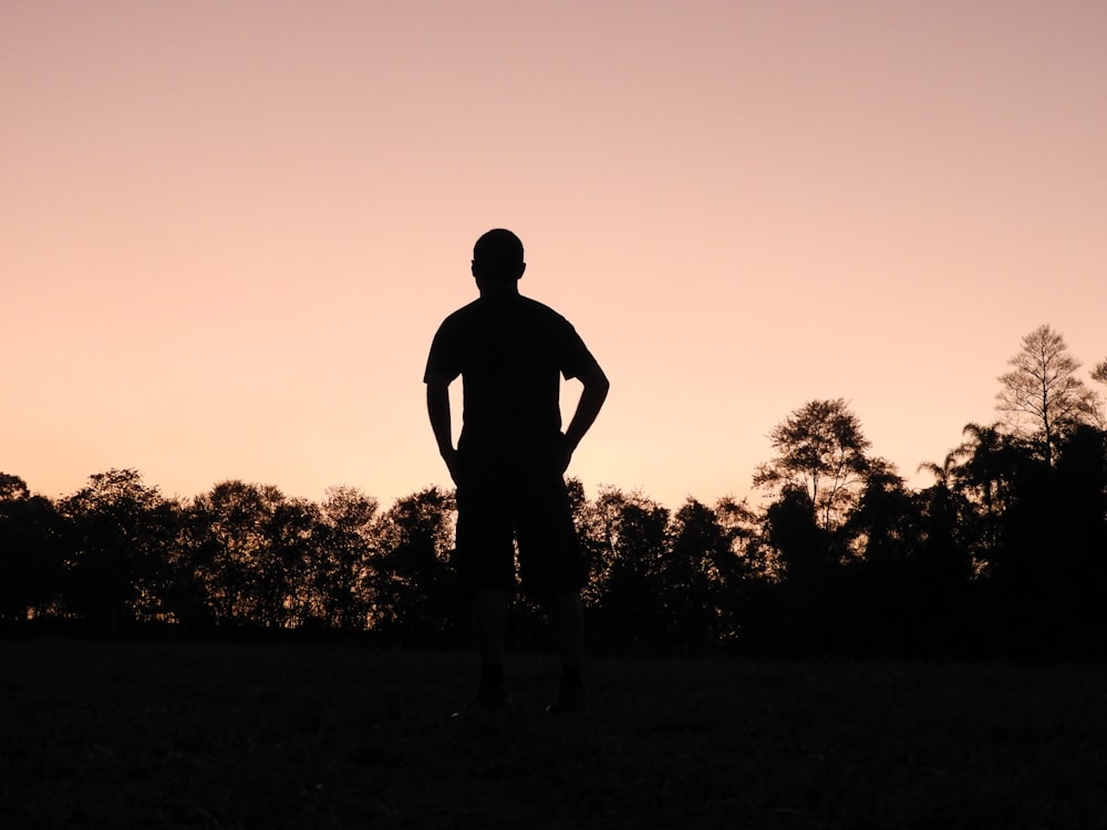 silhouette of man standing on grass field during sunset