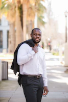 A stylish man in a crisp white shirt and brown trousers walking confidently on a city street.
