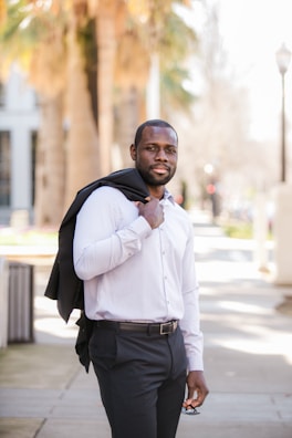 A man wearing a crisp button-down shirt paired with tailored chinos walking through a sunlit city park.