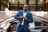 man in blue suit standing beside black car