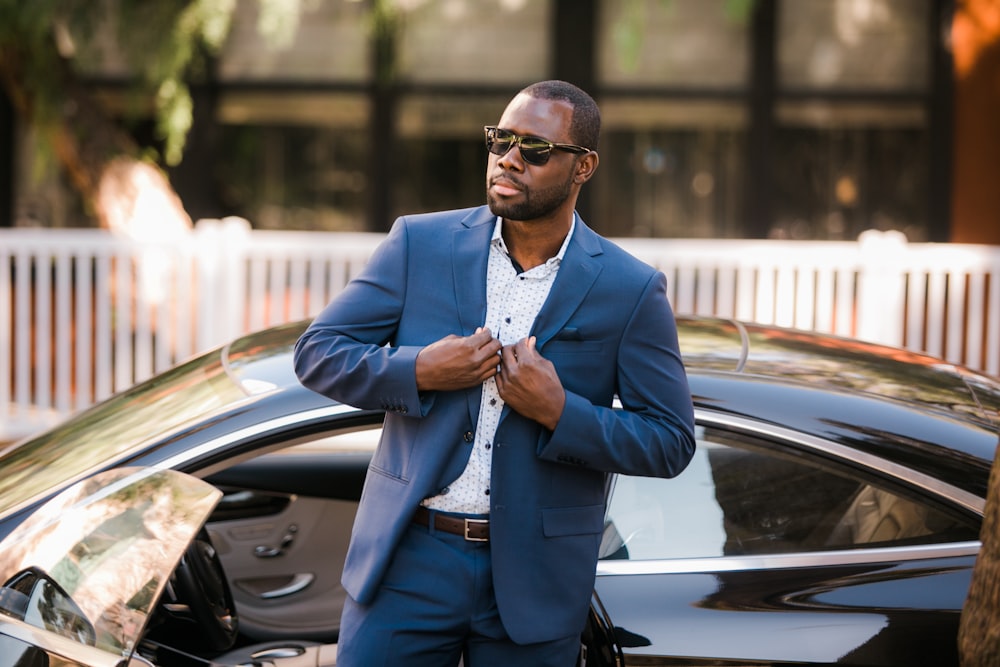 man in blue suit standing beside black car