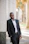 man in black suit jacket leaning on gray concrete wall during daytime