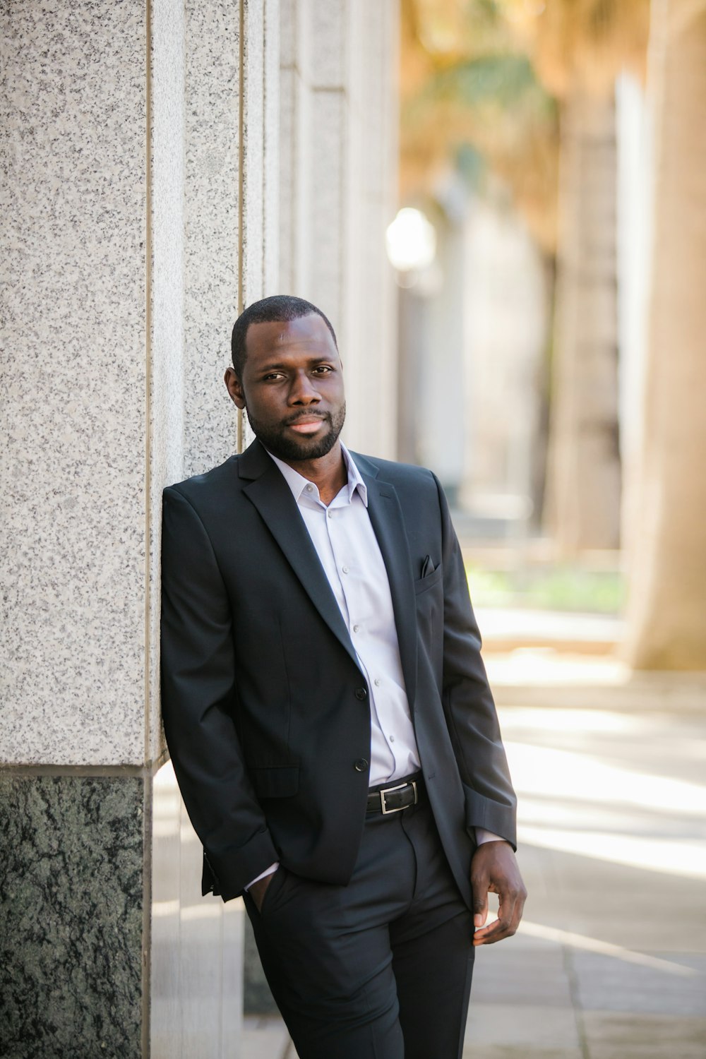 man in black suit jacket leaning on gray concrete wall during daytime