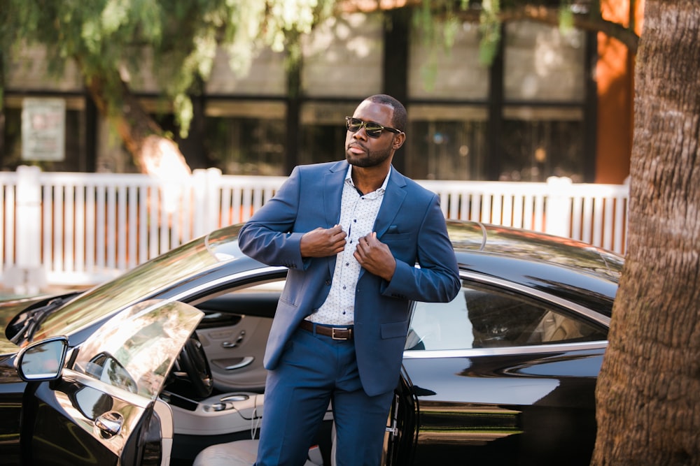 man in blue suit standing beside black car