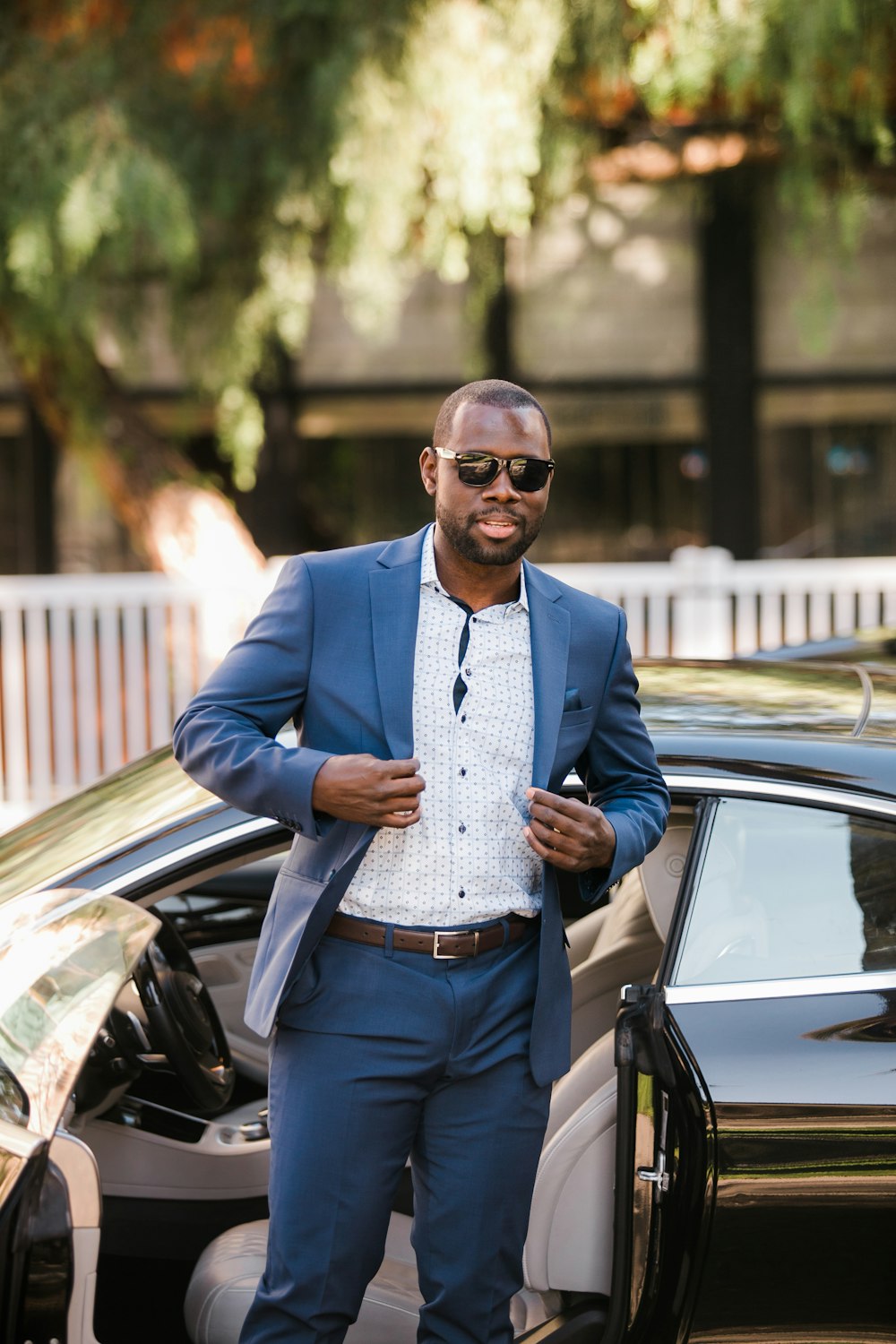 man in blue suit jacket and blue denim jeans standing beside black car during daytime