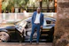 A stylish man in business attire stepping out of a luxury car with a calm, assured expression.