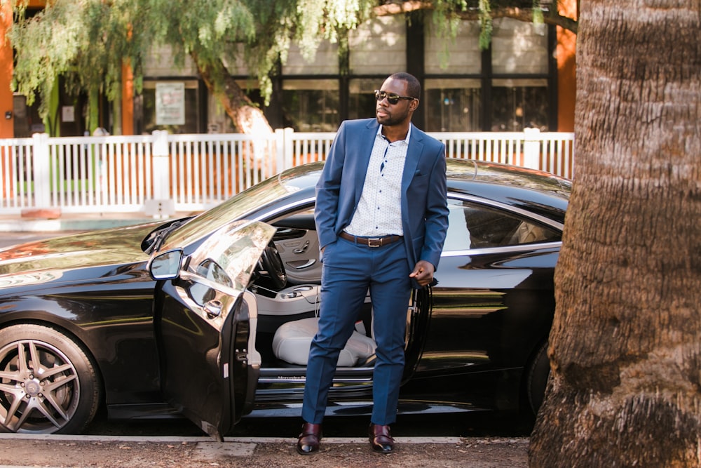 man in white dress shirt and black pants standing beside black car