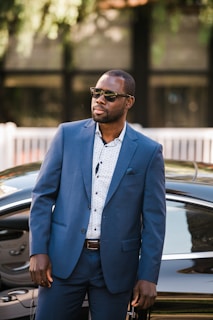 man in blue suit standing beside black car