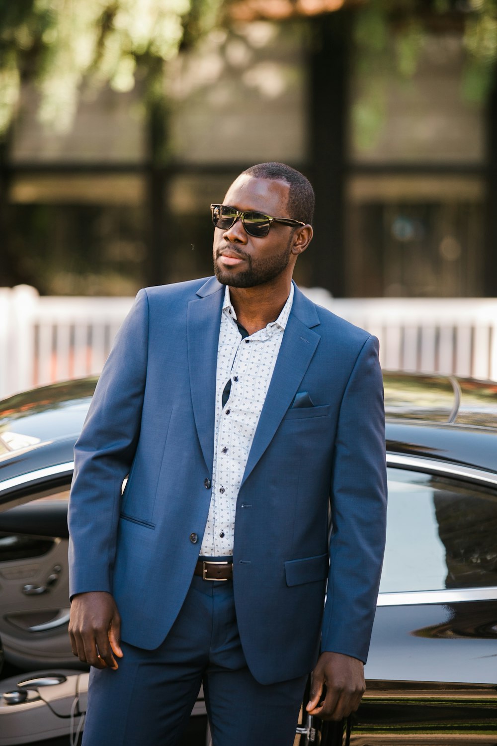 man in blue suit standing beside black car