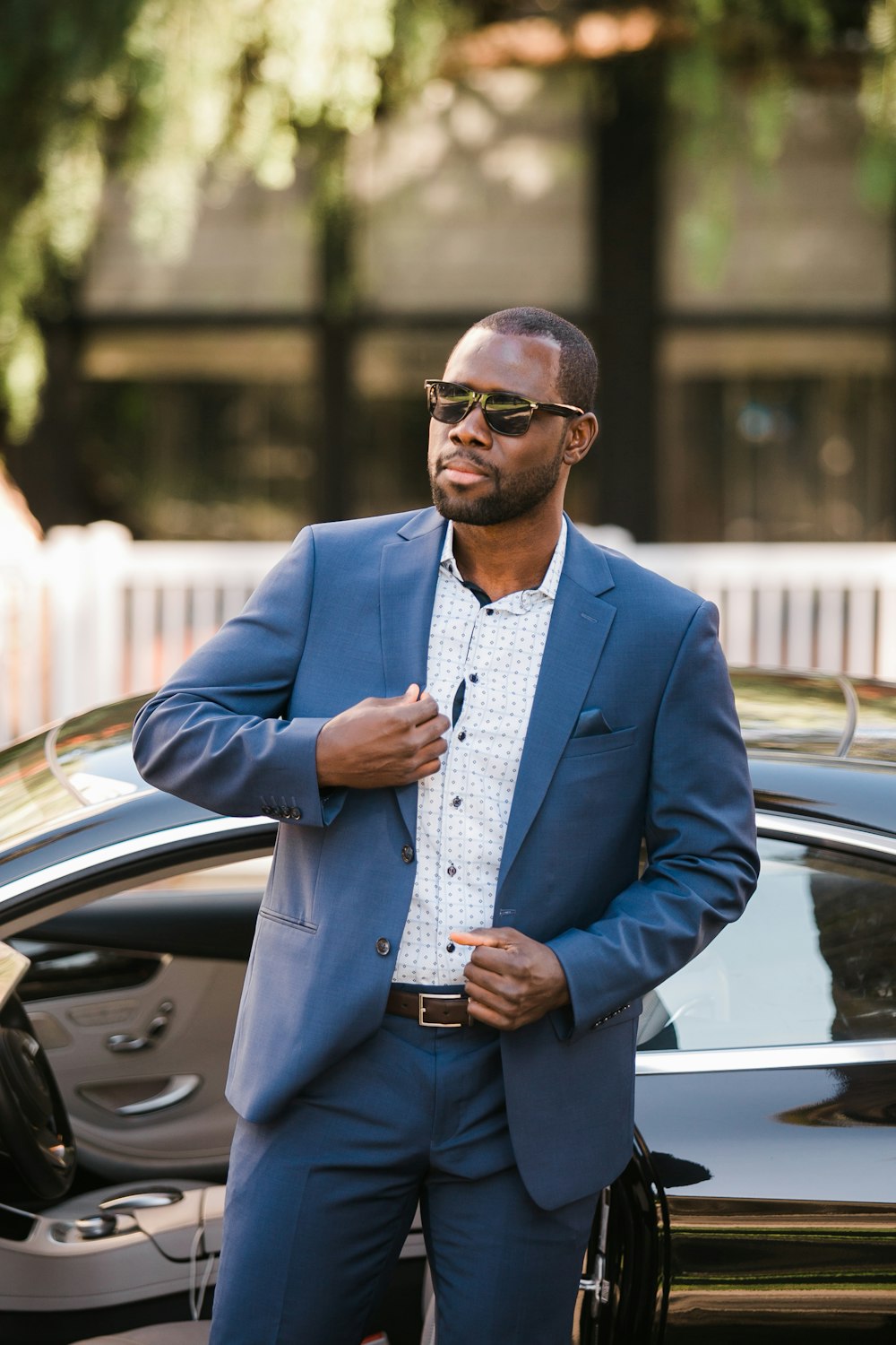 homme en veste de costume bleue et chemise de ville bleue debout à côté d’une voiture noire pendant la journée