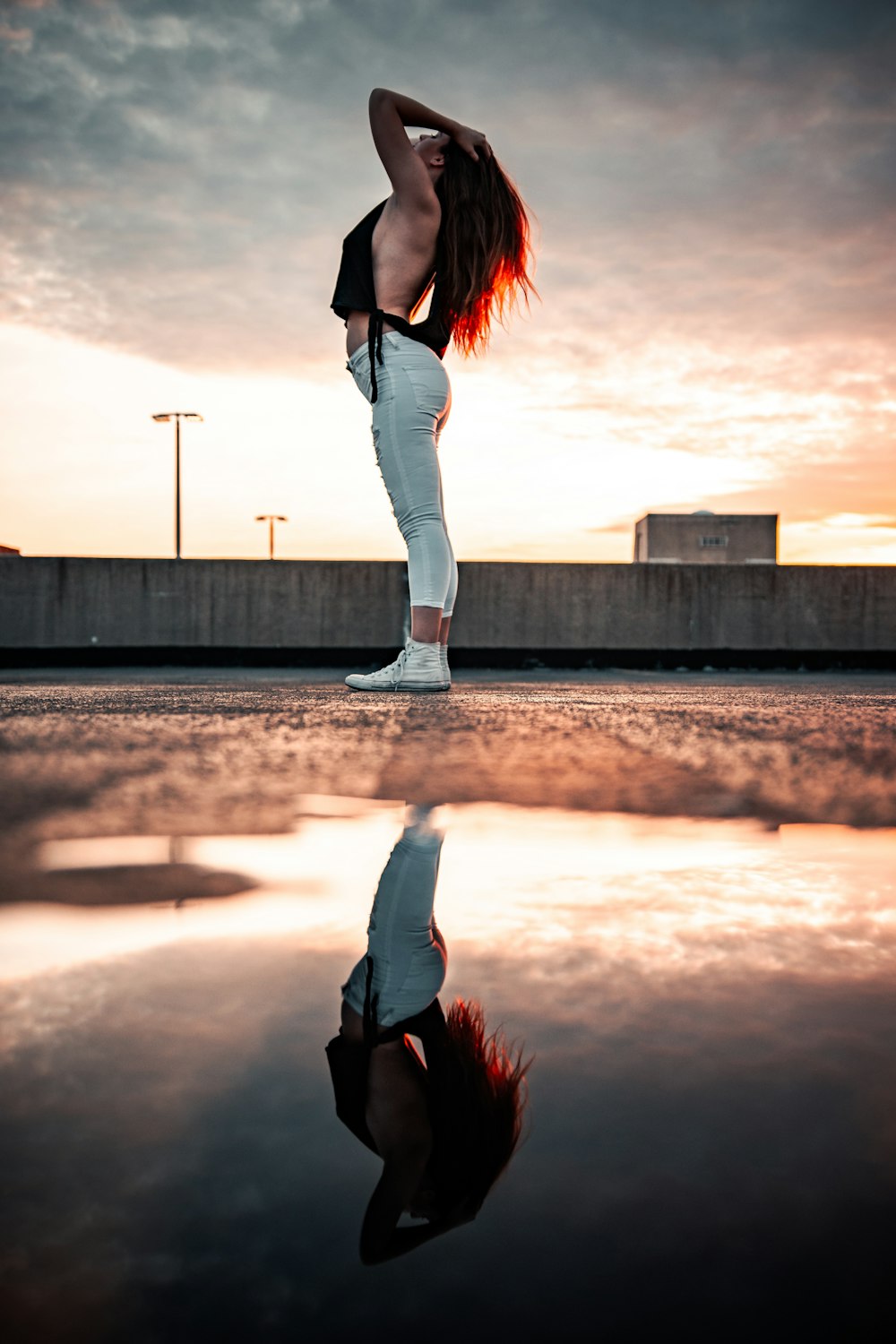 woman in black jacket and white pants standing on gray concrete road during sunset