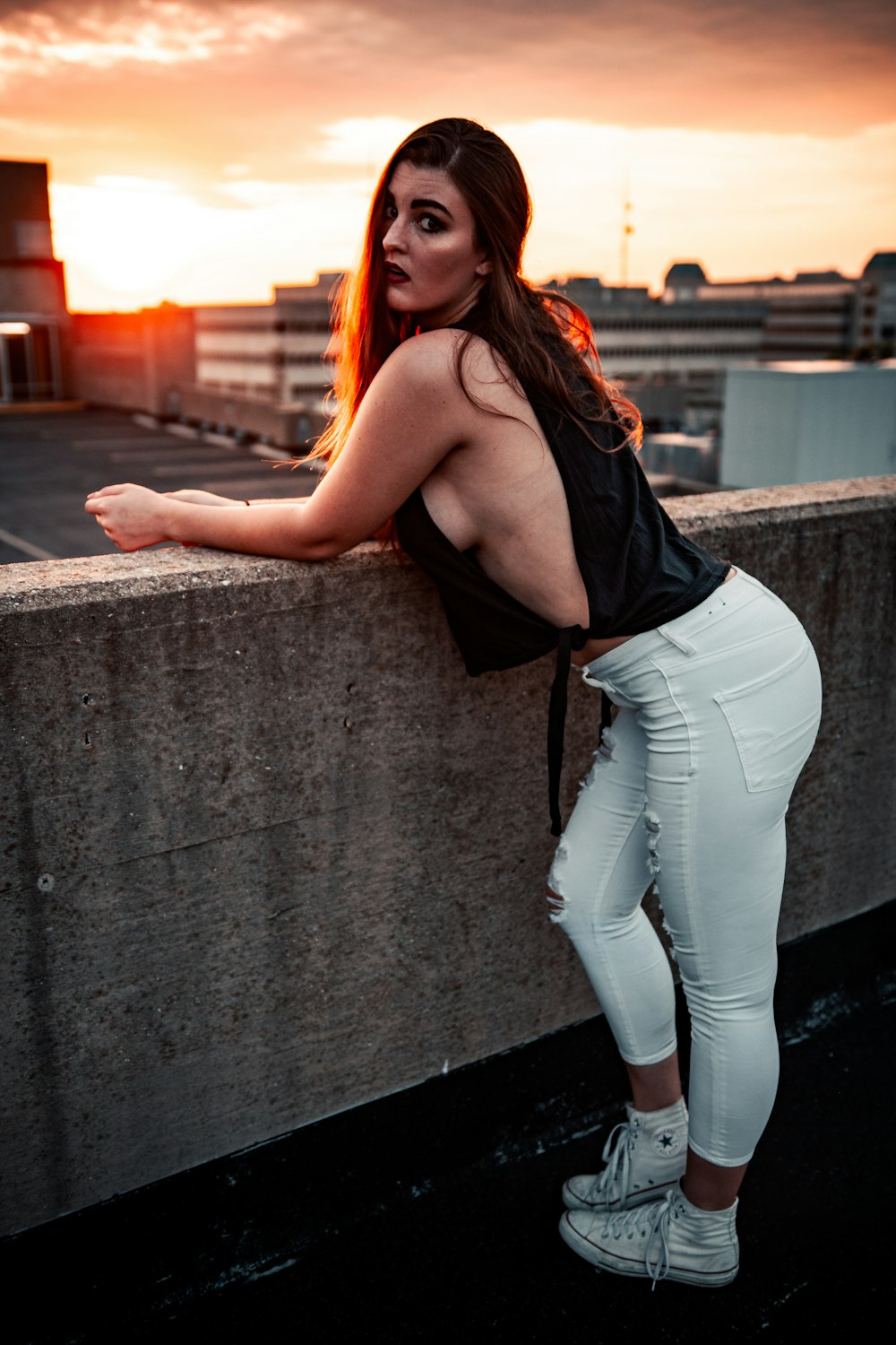 woman in black tank top and white denim jeans leaning on wall during daytime