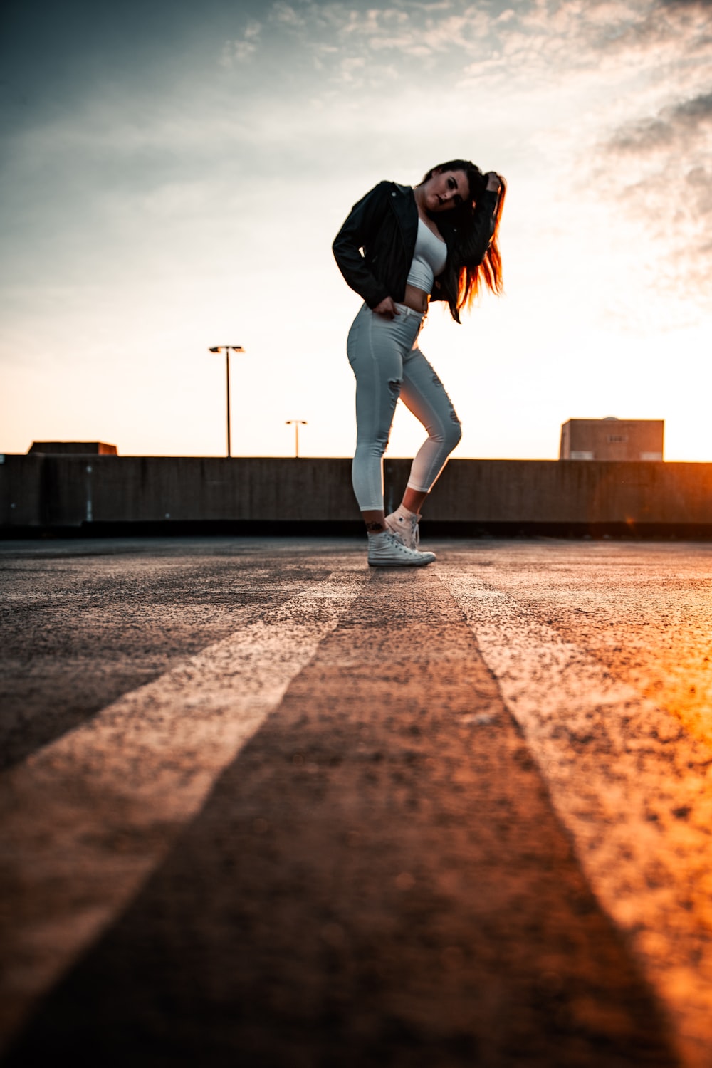 woman in black jacket and white pants walking on gray concrete pavement during daytime
