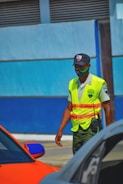 man in yellow and green safety vest and helmet standing beside blue car during daytime